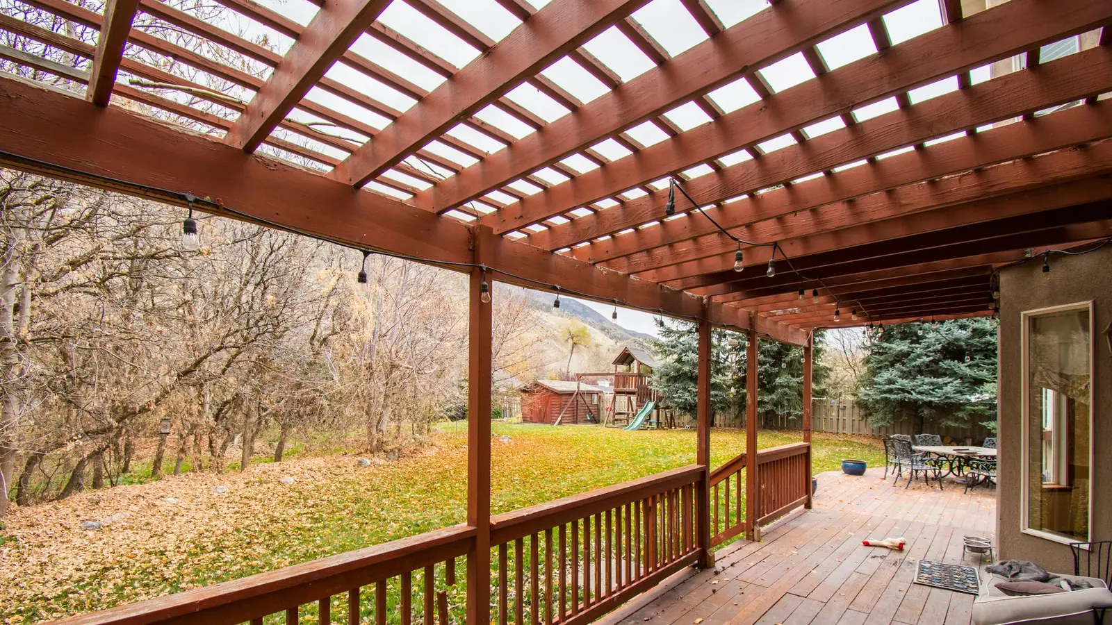 Covered deck with a slatted roof and autumn leaves on the boards
