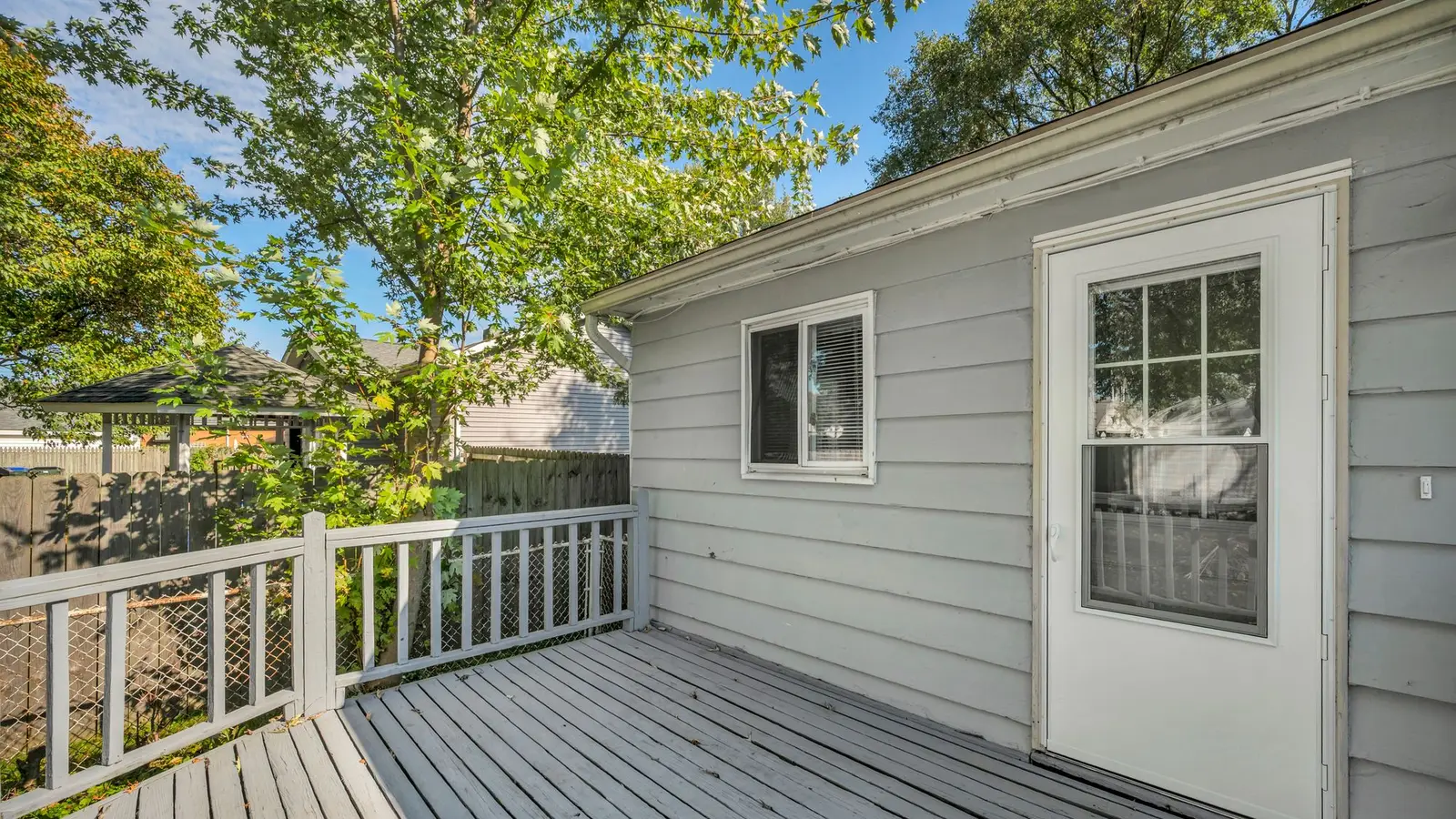 Gray deck with white railings outside a back door of a sided house