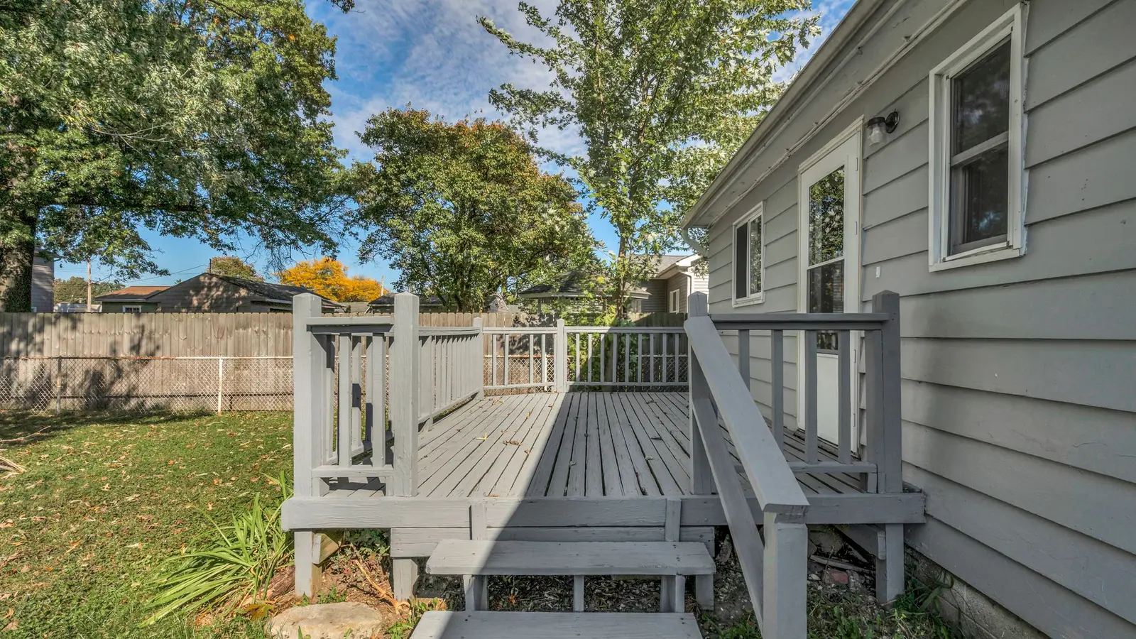 Gray-painted wood deck with railings and steps along the side of a house
