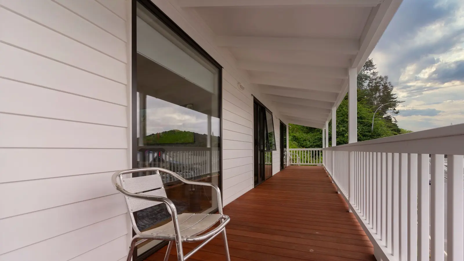 Long porch with smooth reddish-brown deck boards, white railings and a metal chair