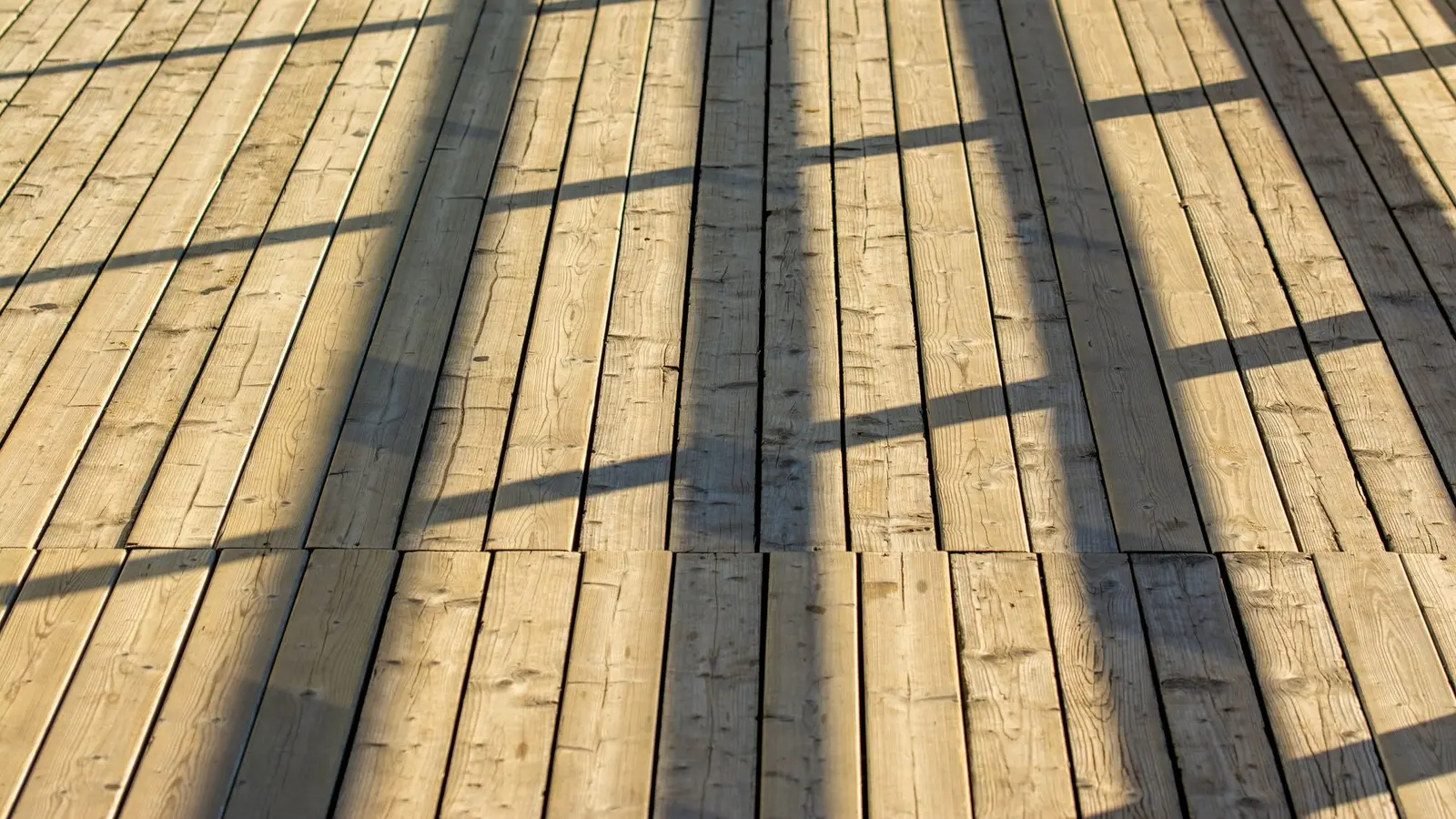 Afternoon sun casting railing shadows across wood deck boards