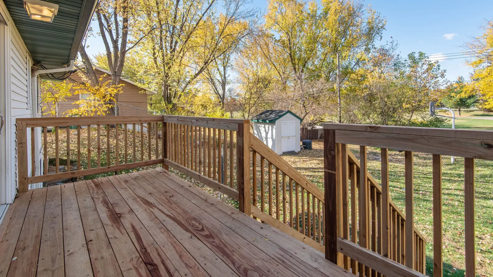 Wood deck with a square-baluster railing overlooking a backyard with autumn trees